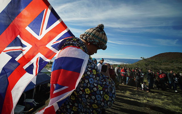 Big Island resident Kalae Kauwe is draped in Hawaiian flags as hula halau dance near the Mauna Kea visitors center.