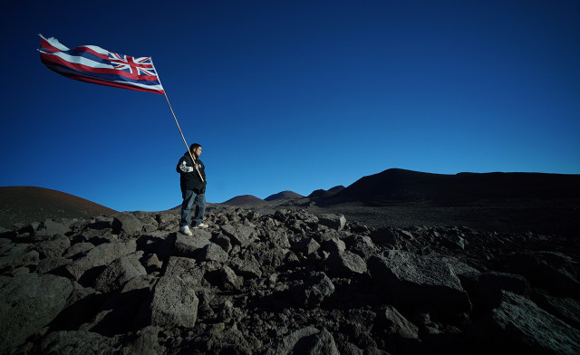Lone demonstrator holds a Hawaiian flag near the summit of Mauna Kea as hundreds of protestors lined the road down at the visitor's center. 24 june 2015. photograph Cory Lum/Civil Beat