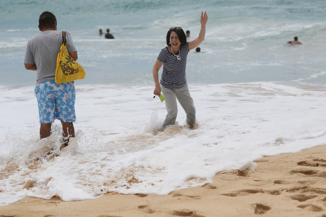Visitors laugh and enjoy an errant shore break wave while not paying attention to the wave sets at Sandy Beach. 