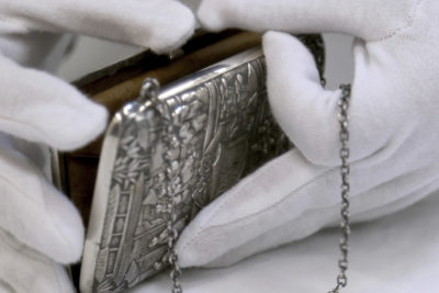 In this Friday, Jan. 26, 2018 photo, an Iolani Palace worker wears gloves to show a silver purse donated to the palace by Abigail Kawananakoa, at Iolani Palace in Honolulu. The 91-year-old Native Hawaiian heiress, Kawananakoa, is fighting her former lawyer over control of her $215 million fortune. Many Native Hawaiians consider Kawananakoa to be the last Hawaiian princess, a tenuous link to when Hawaii was ruled by a royal family. (AP Photo/Caleb Jones)